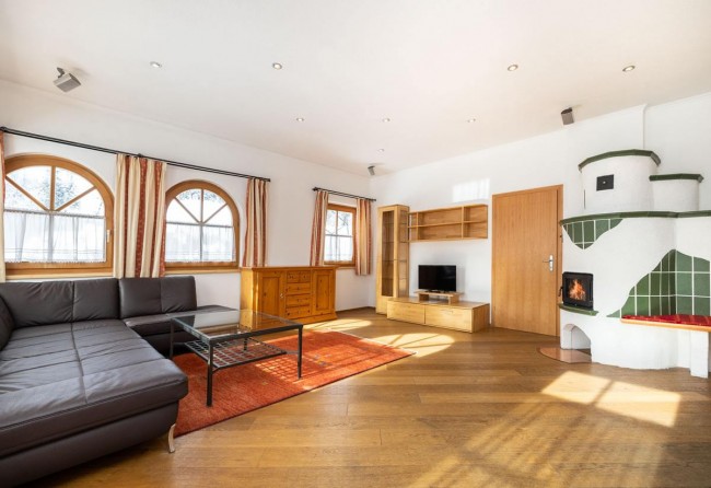Wohnzimmer mit Kachelofen, großer Couch und Flat-TV